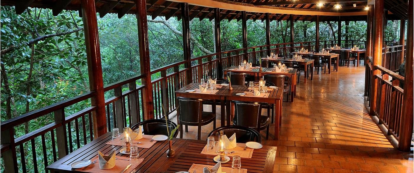 A full view of tables and chairs placed in a steep-tiled outdoor dining area with greenery views | Vythiri Resort, Wayanad